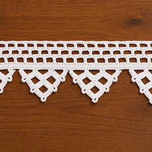 May include: A white crochet lace trim featuring a straight top edge with a repeating rectangular grid pattern and a bottom edge defined by a series of pointed, triangular motifs with open square cutouts and small picot-like decorative edges.