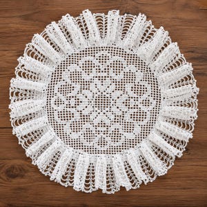 May include: A circular white doily featuring an intricate, openwork grid pattern in the center. The outer edge is finished with a wide, ruffled border composed of delicate, repeating loops and vertical stitches, creating a textured, layered effect.