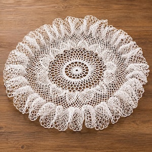 May include: A round white crochet doily featuring an intricate central geometric pattern with a delicate, ruffled, open-work lace border. The circular textile piece displays a fine thread construction with a repeating mesh design throughout the centre.