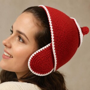 May include: A red crochet hat featuring a white stitched border, rounded ear flaps, and a small pointed top detail. The hat is constructed from a dense yarn texture with a consistent red color throughout and a contrasting white trim along the edges.