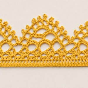 Può includere: Un bordo in pizzo all'uncinetto color giallo senape caratterizzato da un motivo ripetitivo a festoni con complessi anelli traforati e una base dritta solida. Il design tessile mostra una serie di archi e punte interconnesse in filato.