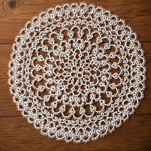 May include: A circular white doily featuring intricate tatting lace work with a repeating floral and geometric pattern. The delicate needlework creates a complex, openwork design that radiates from the centre towards the scalloped outer edge.