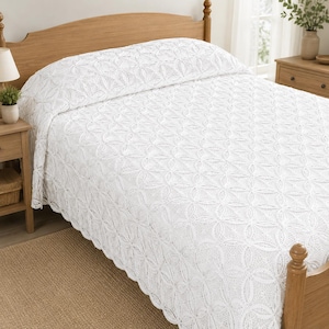 May include: A white bedspread featuring an intricate, repeating circular crochet pattern that covers the entire surface. The textile has a delicate, openwork design with scalloped edges, draped over a bed frame with a wooden headboard and footboard.