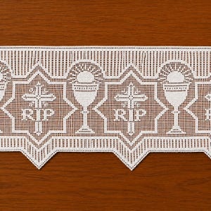以下が含まれることがあります： RIPの文字が入った十字架と聖体拝領の聖杯が交互に並ぶ白いレースのトリム。レース全体に格子状のテクスチャがあり、縁は幾何学的な三角形のパターンで構成されています。この装飾的なレースは、宗教的なモチーフを特徴とする繊細な織り模様で仕上げられています。