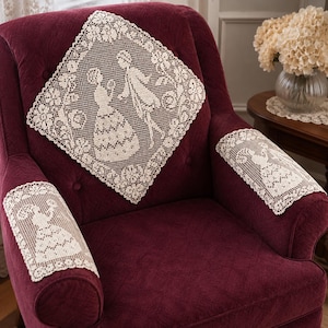 May include: A set of three cream-colored lace doilies featuring intricate floral borders and silhouettes of figures in period clothing. One large diamond-shaped doily is centered on the backrest, while two rectangular doilies cover the armrests.