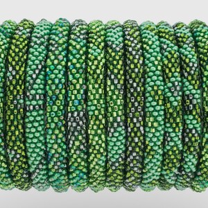 Puede incluir: Una pila de pulseras de cuentas verdes con un degradado de tonos verdes. Las pulseras están hechas de cuentas pequeñas y redondas y tienen un brillo sutil.