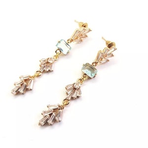 May include: Gold dangle earrings with light blue square stones and clear crystal accents.