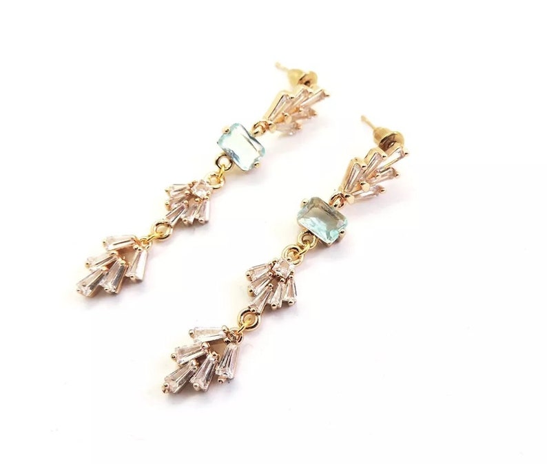 May include: Gold dangle earrings with light blue square stones and clear crystal accents.
