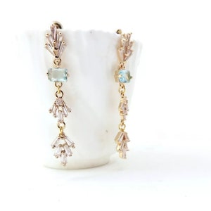 May include: Gold dangle earrings with a light blue gemstone and clear crystal accents.