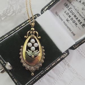 May include: A vintage gold-tone pendant necklace with a teardrop-shaped design. The pendant features four small pearls and a floral motif. The necklace is displayed in a dark green velvet jewelry box with the text "A. ROBERTS" and "199. EDGWARE R. LONDON" visible.
