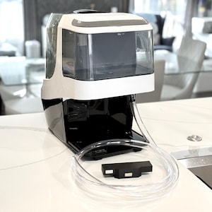 May include: A white and black appliance with a clear water reservoir. A clear tube and a black rectangular component are in front of the appliance. The appliance is on a white countertop.