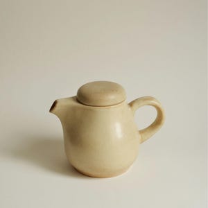 Tetera de estudio, estilo vintage moderno de mediados de siglo: jarra de cerámica minimalista escandinava color crema mate, tetera de gres terroso con tapa ajustada.
