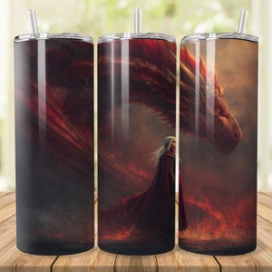 May include: A set of three stainless steel tumblers with a fantasy-themed design. The design features a red dragon, a person in a red cloak, and a fiery background. Each tumbler has a silver lid and a clear straw.