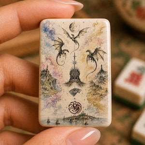 May include: A rectangular tile featuring a detailed illustration of three dragons, a central throne, a sword, a wolf emblem, and a circular dragon crest. The artwork includes a moon, a castle on a cliff, and a coastal city with ships in a watercolor style.