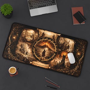 May include: A rectangular desk mat featuring a sepia-toned fantasy illustration with multiple scenes, a central ring motif, and the text 'Not all those who wander are lost.' The design includes a volcanic landscape, a tower, and various figures.