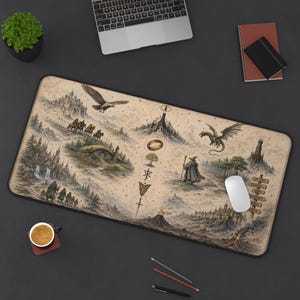 May include: A rectangular desk mat featuring a detailed fantasy map illustration in muted earth tones. The design includes a central vertical column of symbols, a flying eagle, a dragon, a wizard, a hobbit hole, and various mountain landscapes.