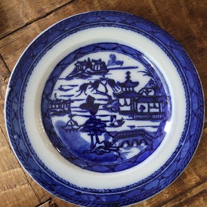 Puede incluir: Un plato de porcelana azul y blanco con un diseño de paisaje chino. El plato tiene un borde azul y blanco con un diseño de cuerda.