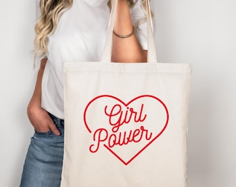 May include: A white canvas tote bag with red text that says "Girl Power" inside a red heart.