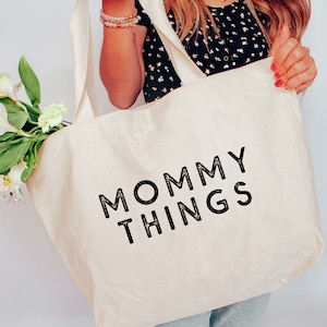 Puede incluir: Una bolsa de lona blanca con texto negro que dice "Mommy Things".