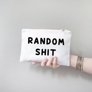 May include: White canvas pouch with a zipper closure. The pouch has black text that reads "RANDOM SHIT".