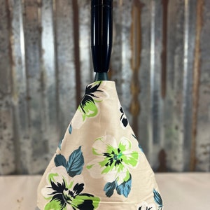 May include: A beige, white, green, and blue floral patterned car shift boot with a black shift knob.