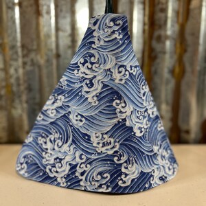 May include: A blue and white lampshade with a wave pattern. The lampshade is cone-shaped and has a white cord.