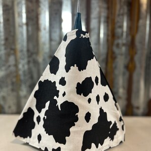 May include: A black and white cow print fabric cone shaped hat with a black plastic antenna on top.