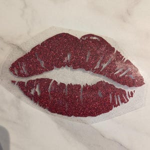 Puede incluir: Un dise&ntilde;o de labios rojos con purpurina sobre un fondo transparente. Los labios son de color rojo intenso y est&aacute;n llenos de purpurina. El dise&ntilde;o es probablemente para manualidades o decoraci&oacute;n de ropa.