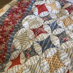 May include: A patchwork quilt featuring a cathedral window design with various fabric patterns. The quilt displays red floral prints, blue and white stripes, yellow and white stripes, and small floral motifs in a repeating circular arrangement.