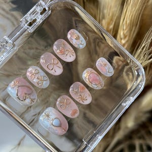 ピンクとライトブルーの手作りかわいいプレスオンネイル。ゴールドのリボンとハートのアクセントがかわいいショート丈。