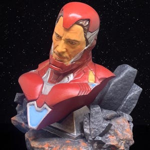 May include: A red, white and silver Iron Man bust figurine with a detailed face and a rocky base.