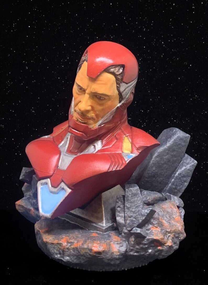 May include: A red, white and silver Iron Man bust figurine with a detailed face and a rocky base.
