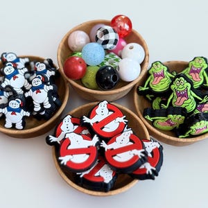 May include: Wooden bowls filled with colorful beads and charms. The collection includes Stay Puft Marshmallow Man, Ghostbusters logo, Slimer, and various round beads in multiple colors and patterns.