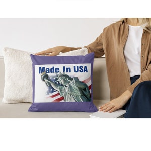 May include: Purple throw pillow with a white background featuring a depiction of the Statue of Liberty and the words "Made in USA".