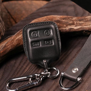 May include: Black leather key fob cover with embossed buttons and a silver-tone metal clasp. Includes a matching leather strap with a metal D-ring. The key fob cover is designed to protect car keys.