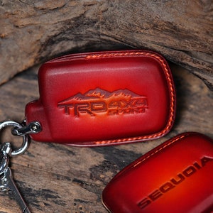 May include: Two red leather keychains with stitching. One keychain has the text "TRD 4X4 Sport" and the other has the text "SEQUOIA".