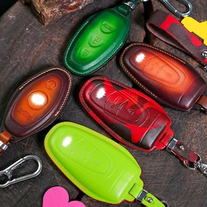 May include: Five leather key covers in different colors and patterns. The covers are designed to protect car keys and have a key ring attached.