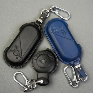May include: Three key fobs with leather covers. One is black, one is blue, and one is black with a circular button. The blue fob has a silver loop and a silver clip. The black fobs have silver loops.