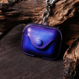 May include: A blue leather case with a silver keychain attached. The case has a flap with a button closure. The case is sitting on a wooden surface.