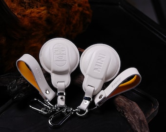 May include: Two white leather keychains with metal rings. One keychain has the word "MINI" printed on it and the other has the word "POPPY" printed on it.