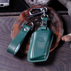 May include: A green leather key chain with a key fob and a loop for attaching to a belt or bag.