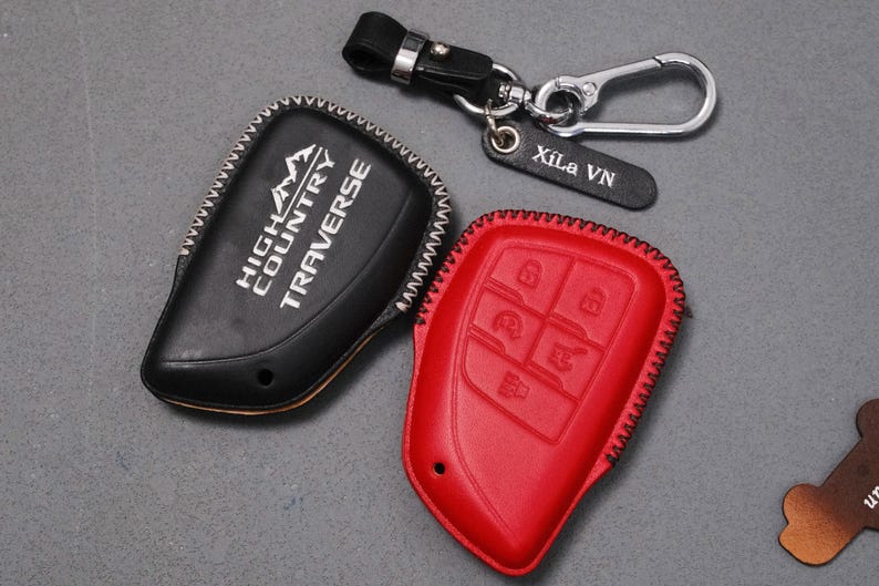 May include: A black leather key fob cover with "HIGH COUNTRY TRAVERSE" in white lettering, and a red leather key fob cover with embossed buttons. A keychain with a leather tag that says "Xila VN" is also included.