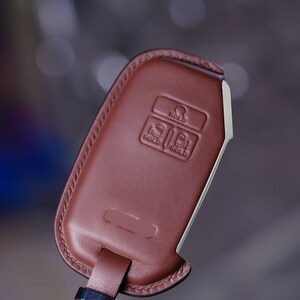 May include: A brown leather key fob with a silver metal key ring. The fob has three buttons labeled "HOLD", "HOLD", and "HOLD".