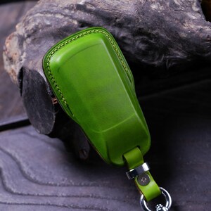 May include: A green leather key fob with a silver metal ring and a green leather strap. The fob is stitched with a light brown thread.