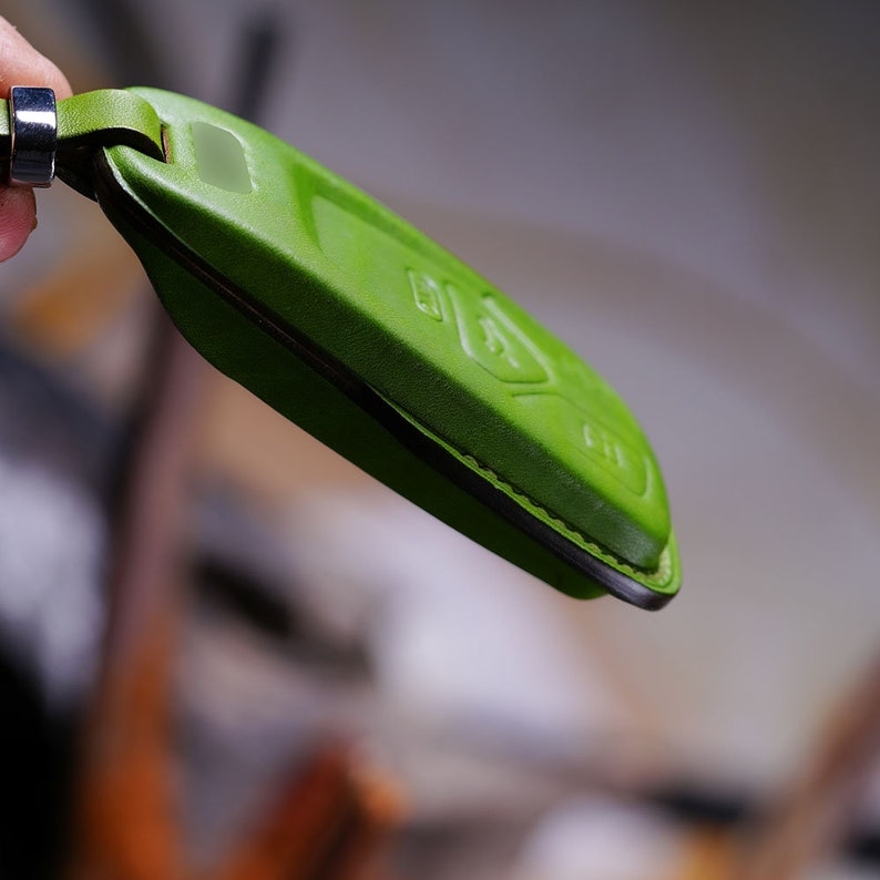 May include: A green leather key fob with a stitched seam. The fob is designed to protect a car key.