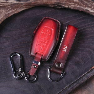 Może przedstawiać: Czerwony skórzany brelok do kluczy ze srebrnym kółkiem i pasującym czerwonym skórzanym paskiem z wytłoczonymi inicjałami "MJ".