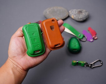 May include: Two green leather key covers with buttons and a brown leather key cover. The key covers are on a gray surface.