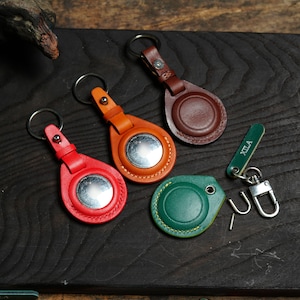 Puede incluir: Cuatro llaveros de cuero con anillos de metal. Los llaveros tienen forma de lágrima con un inserto de metal circular. Los llaveros son marrones, naranjas, rojos y verdes.