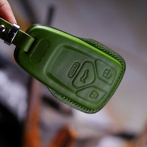 May include: Green leather key fob with four buttons. The buttons are labelled with symbols for unlock, lock, boot, and panic.