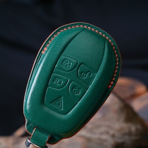 Pode incluir: Chaveiro de couro verde com costuras laranja. O chaveiro tem cinco botões com símbolos em relevo.